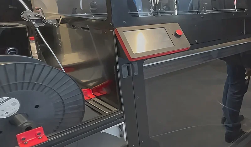 3D printer Modix Big-180x with touchscreen panel, large filament spool, and sleek black design in a workshop setting.