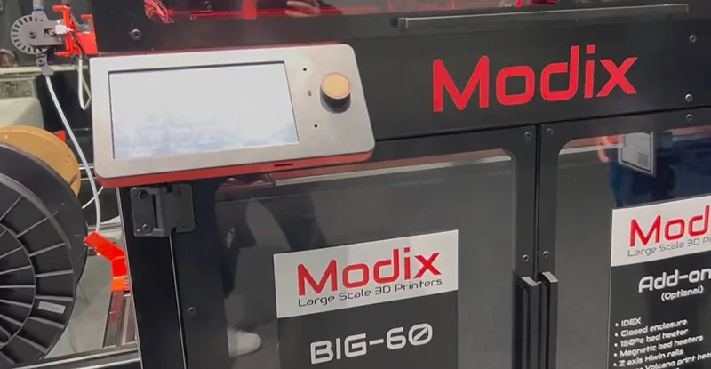 Modix Big 60 3D printer with control screen, branding, and parts visible in an industrial setting, emphasizing its large-scale printing capabilities.