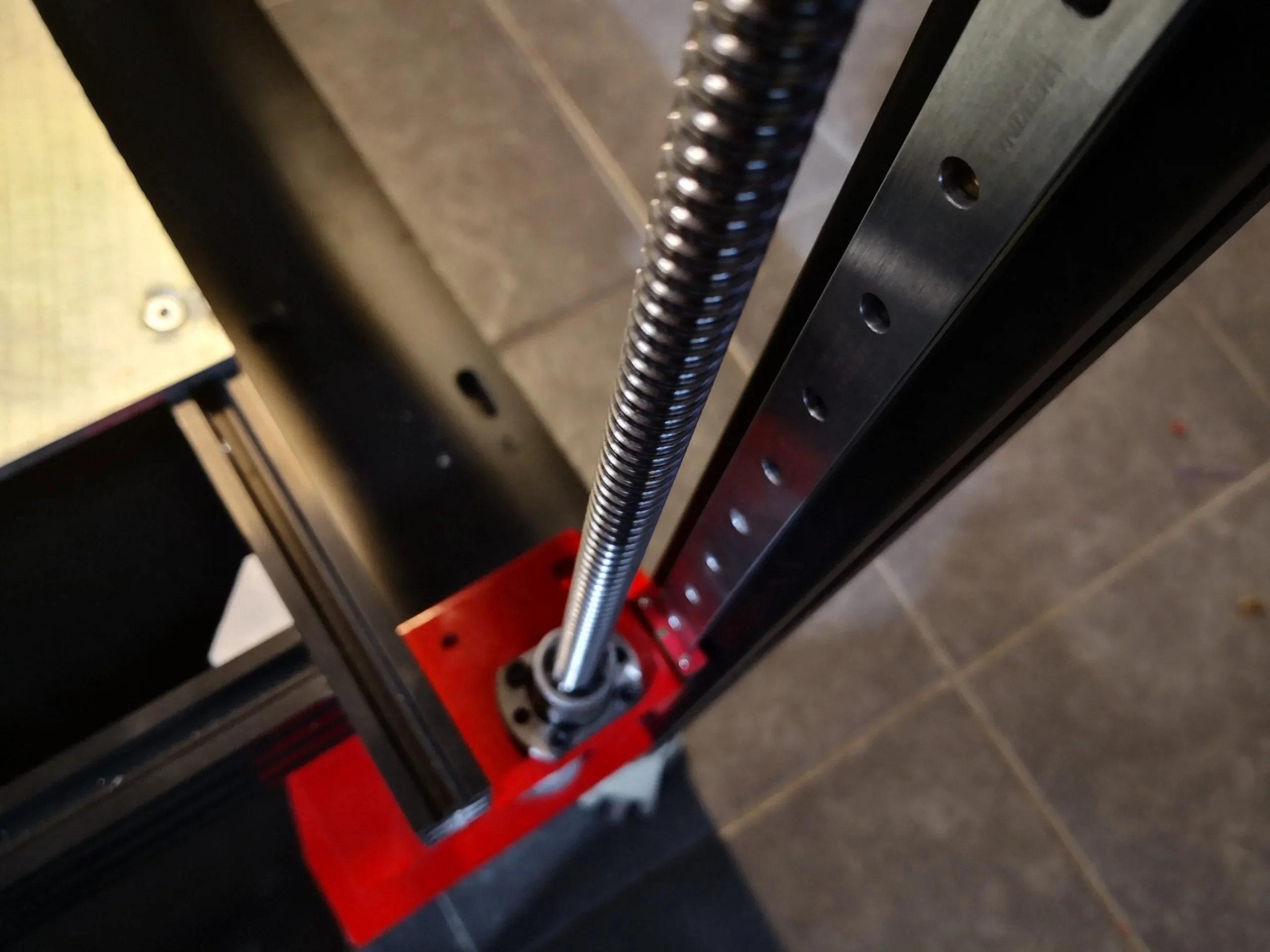 Close-up of Modix Big 60 3D printer's Z-axis lead screw and linear rail assembly, set against a tiled floor.