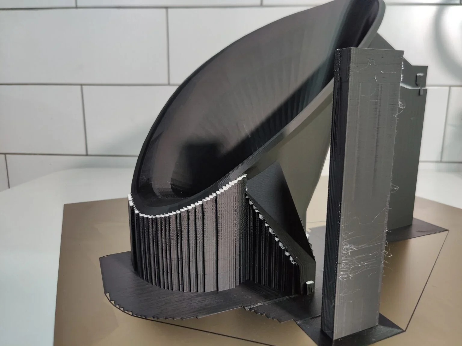 Black 3D-printed architectural part on a flat surface, created by Modix Big 60. Features clean lines and complex support structures.