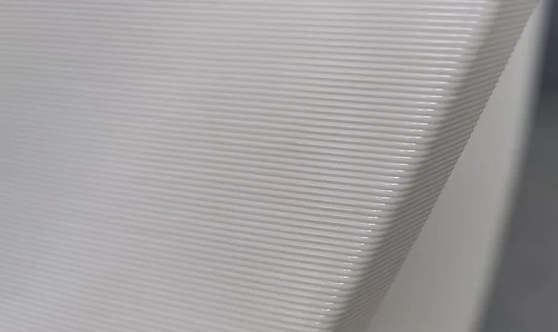 Close-up of a smooth white 3D printed surface with horizontal lines made by the Modix Big Meter printer, showcasing precision printing detail.