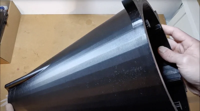 Large black 3D-printed cone part held on wooden table, created using Modix Big Meter, showcasing precise layers and smooth surface texture.