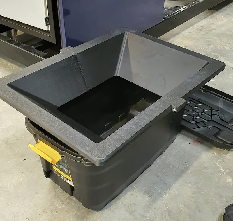 Modix Big Meter-printed large black container with an open lid, featuring a thick rim and visible locking mechanism, on a concrete floor.