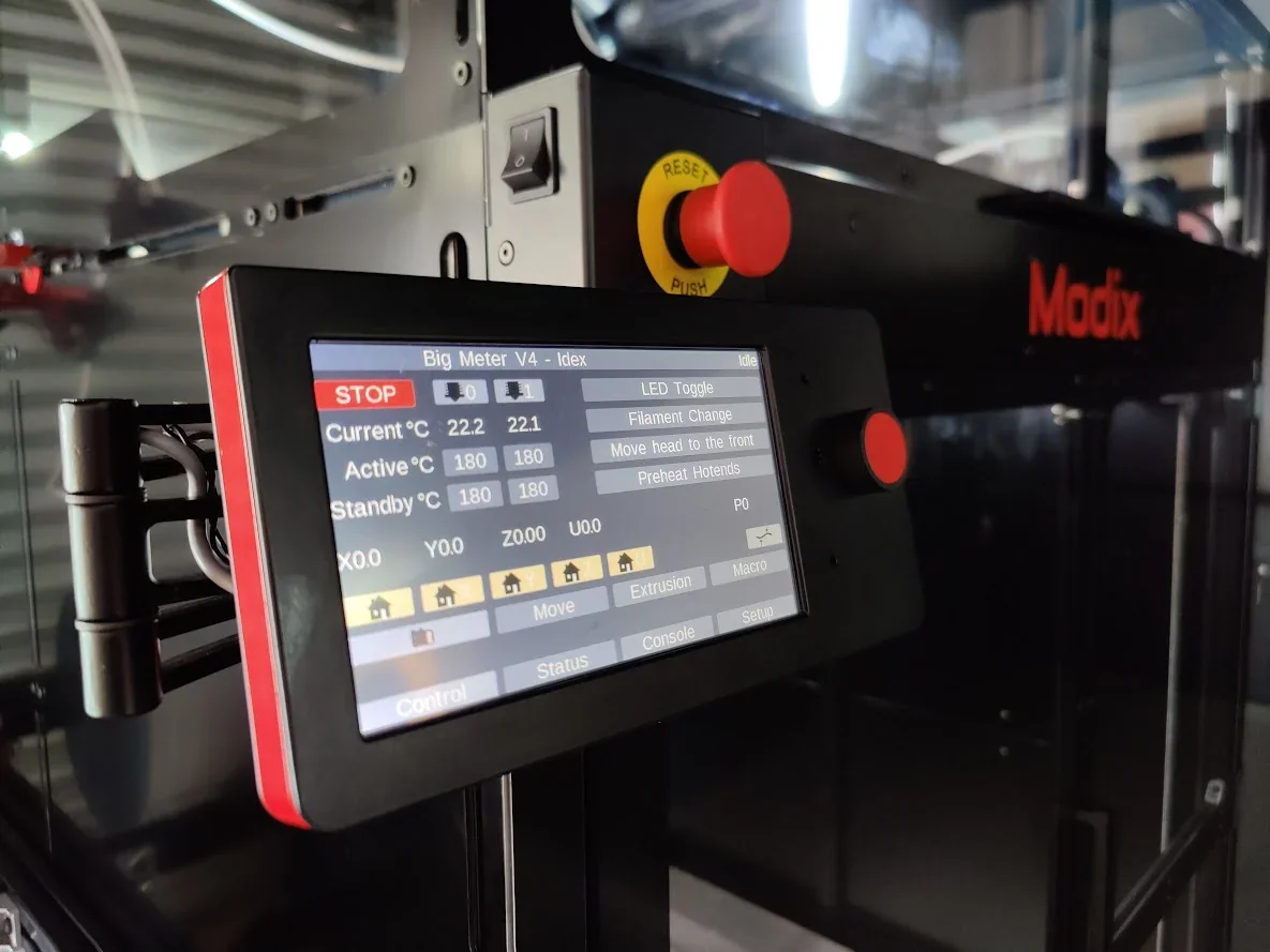 Modix Big Meter 3D printer with touchscreen displaying settings, enclosed in a sleek black casing with visible Modix branding, in an industrial setting.