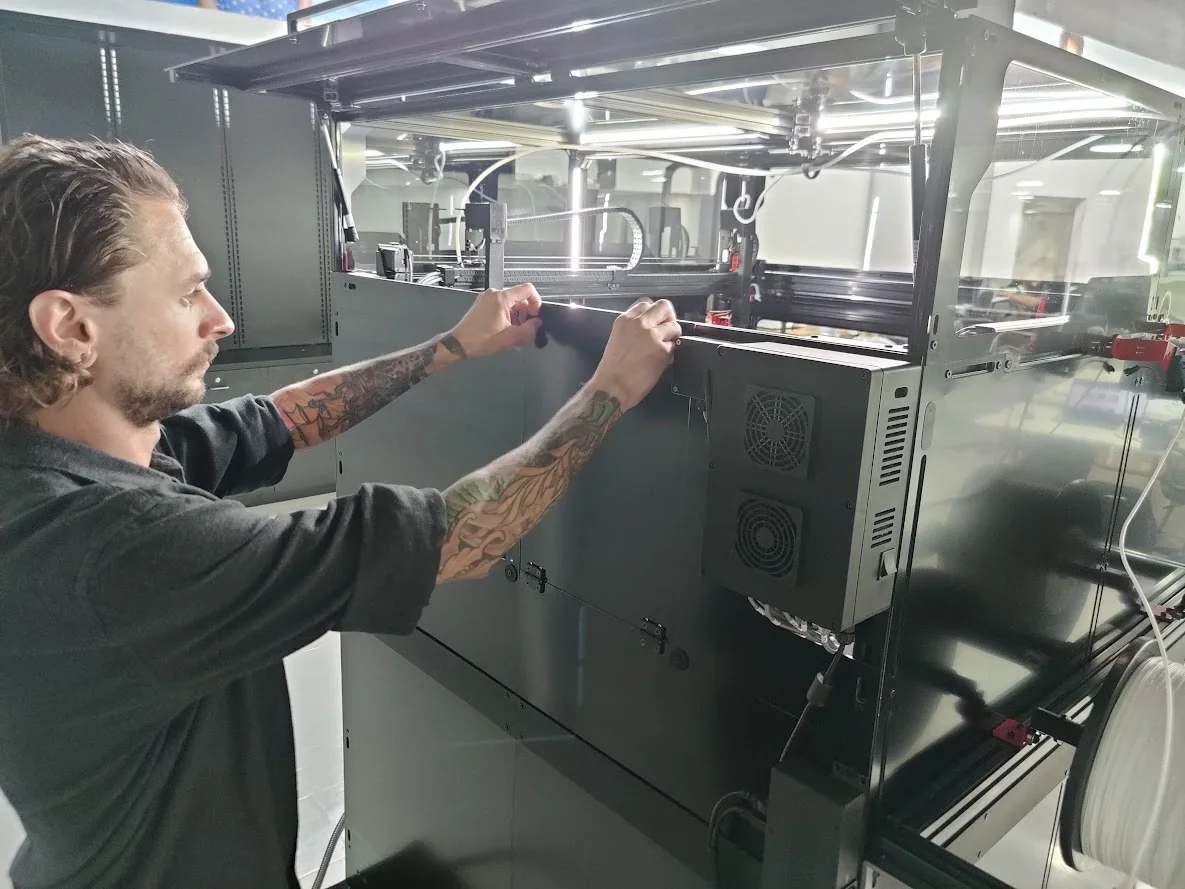 Technician adjusting Modix Big Meter 3D printer in a workshop, featuring large build volume and visible components.