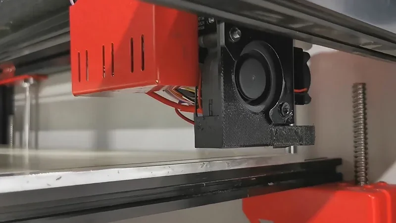 Modix Big Meter 3D printer close-up showing extruder nozzle and wiring, with red and black components in an industrial setting.
