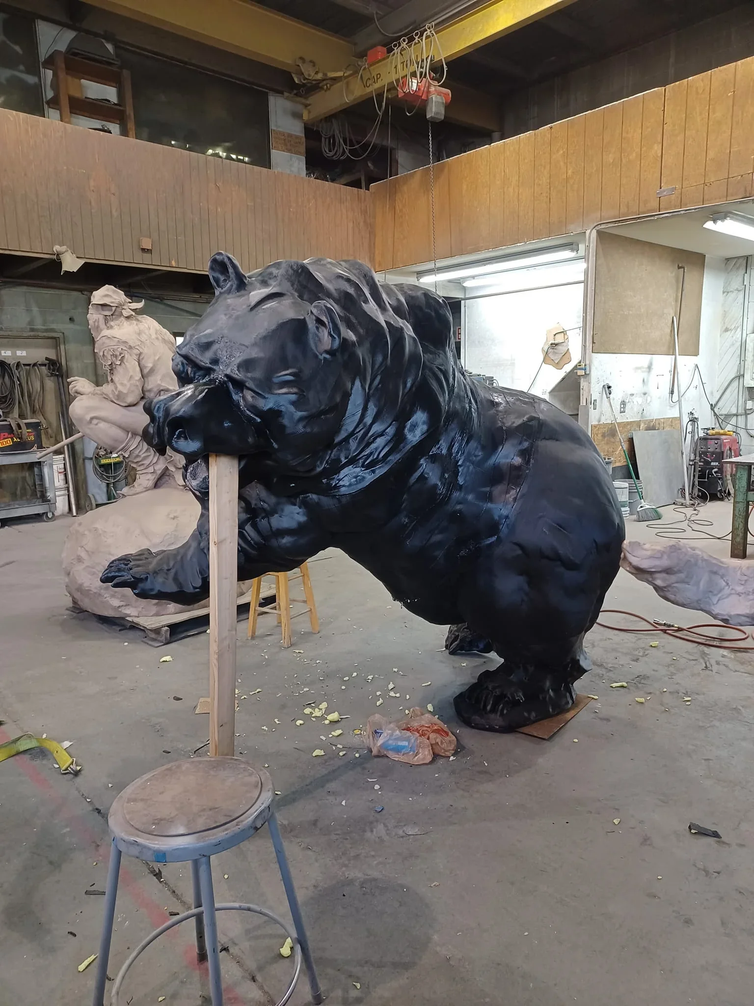 Giant black bear sculpture created by Modix Big Meter 3D printer in a workshop, surrounded by tools and another sculpture in progress.