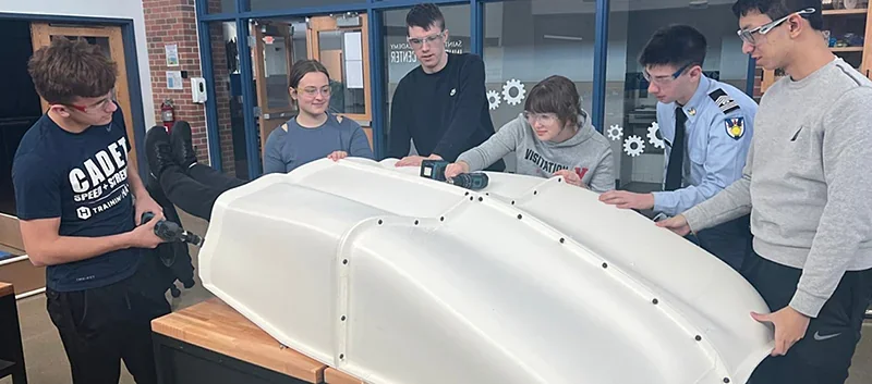 Group of people examining large 3D printed car part created by Modix Big Meter in a workshop setting.