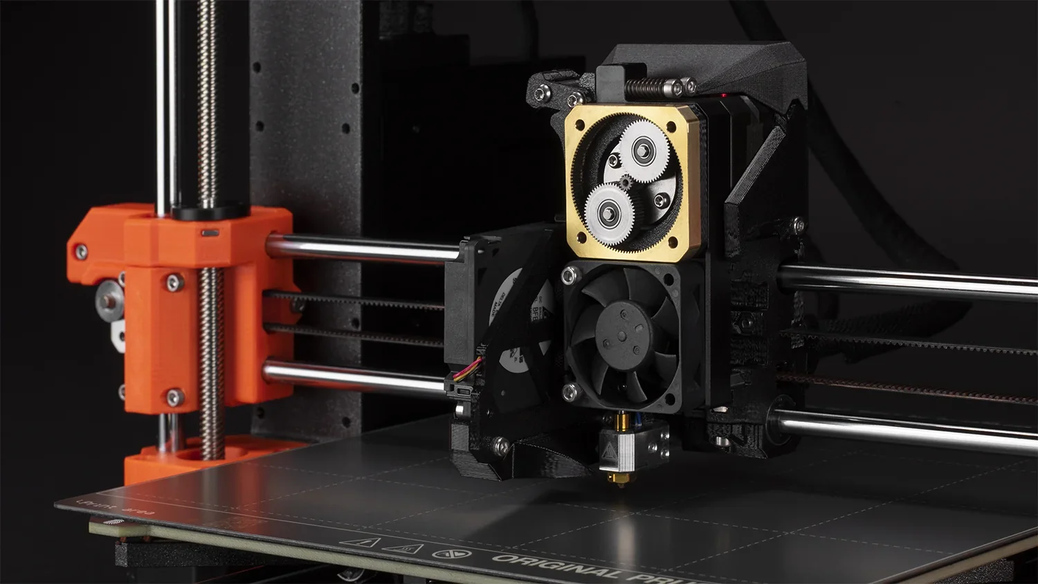 Original Prusa MK4S 3D printer kit showing extruder mechanism and heated print bed with visible branding on a dark background.