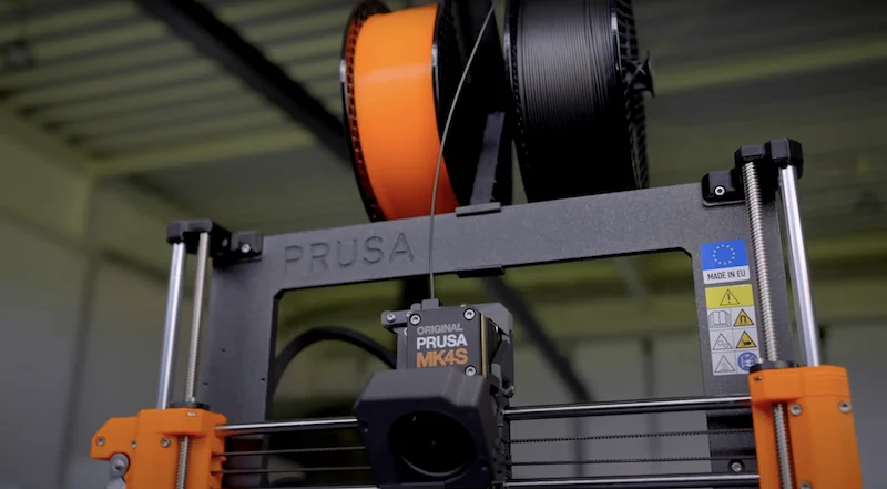 Original Prusa MK4S 3D printer with filament spools on top, displaying EU branding and technical labels, set in an industrial environment.