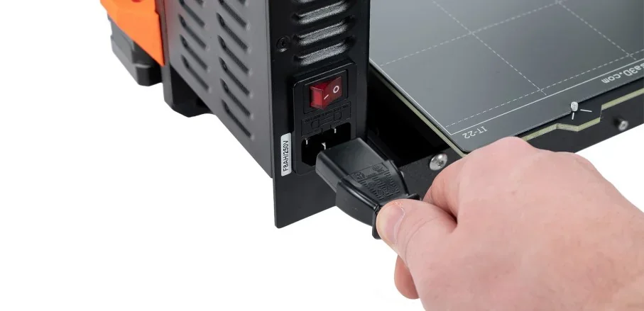 Hand plugging power into Original Prusa MK4S 3D Printer Kit, showing power switch and build platform in a close-up view.
