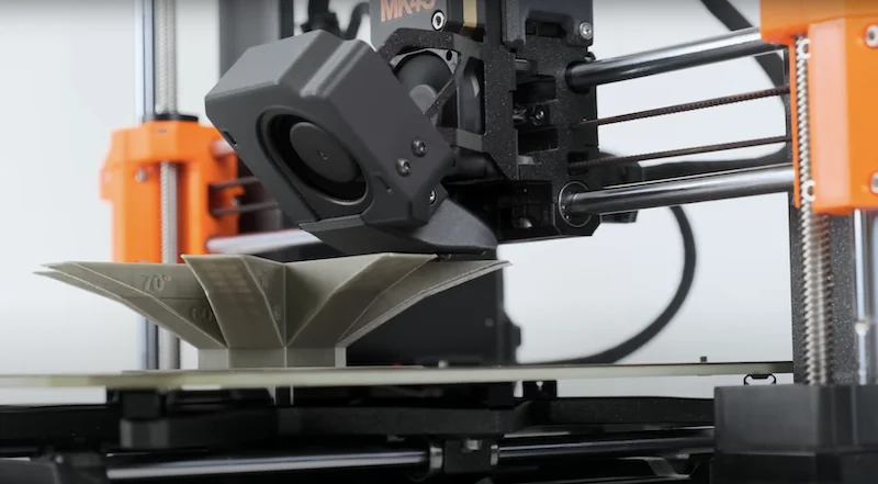 Original Prusa MK4S 3D printer kit creating a detailed model. Features include sturdy frame and precise extruder components working together efficiently.