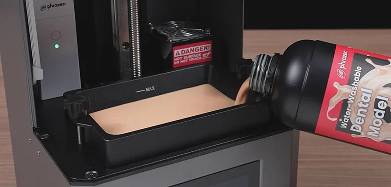 Phrozen Lumii DLP 3D printer being filled with water-washable dental model resin, showcasing the open printer tray and branding.