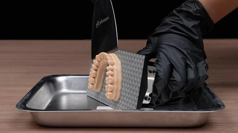 Phrozen Lumii DLP printing dental molds on metal plate; gloved hand holds tray; phrozen logo visible; dark wood table backdrop.