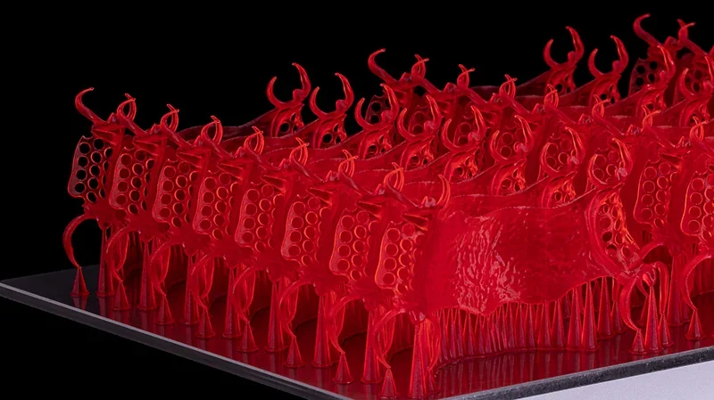 Red 3D-printed models of intricate shapes created by Phrozen Sonic CS+ on a reflective surface, showcasing precision and detail in design.