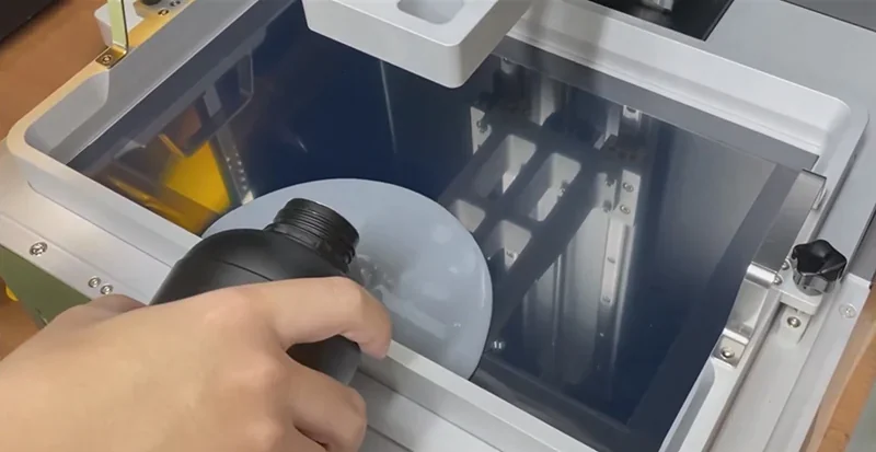 Hand pouring resin into Phrozen Sonic Mega 8K V2 3D printer, showing machine's build plate.