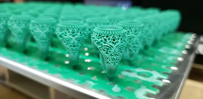 Multiple intricate green resin rings on a 3D printer build plate, created by the Phrozen Sonic Mega 8K V2, showcasing detailed craftsmanship.