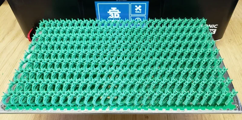 Green 3D-printed figures on a platform from the Phrozen Sonic Mega 8K V2. The machine's branding is visible in the background.