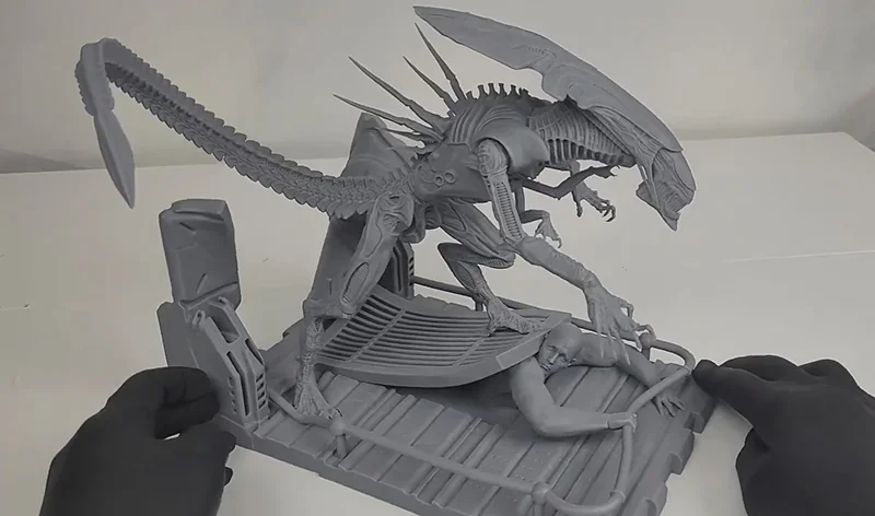 Phrozen Sonic Mega 8K V2 3D print of a detailed alien creature on a platform, showcasing intricate design and precision, handled by gloved hands.