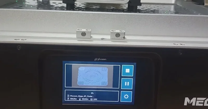 Phrozen Sonic Mega 8K V2 3D printer displaying print status on screen, manufacturing intricate part; silver platform and branding visible.