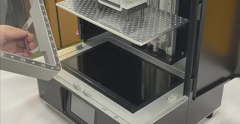 Phrozen Sonic Mega 8K V2 open, showcasing build platform and resin vat. A hand holds a component, indicating replacement or setup.