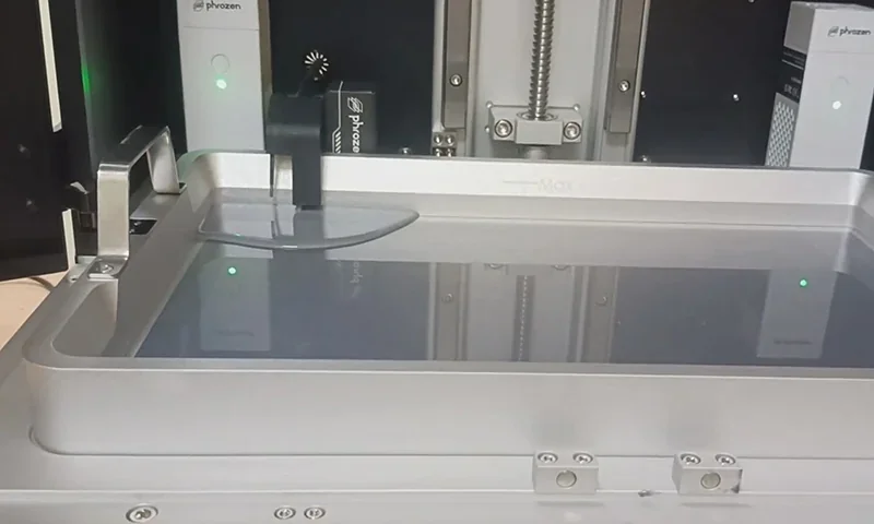 Phrozen Sonic Mega 8K V2 printer's build platform and resin vat, showcasing precision mechanics, internal components, and branding details in a workshop setting.