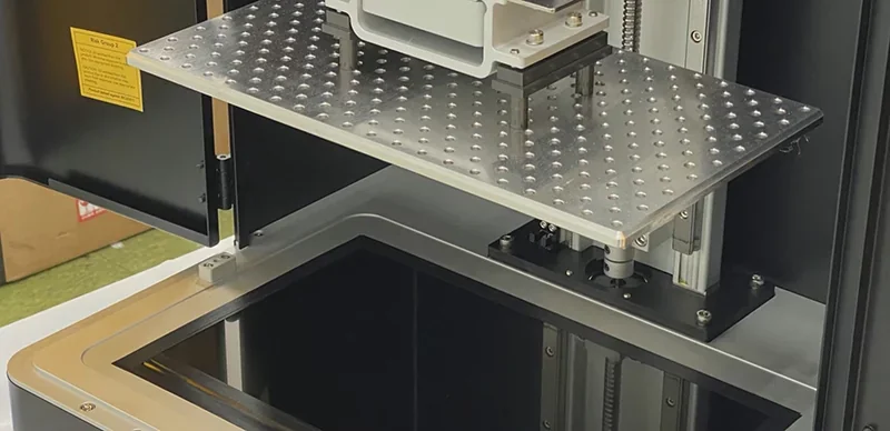 Phrozen Sonic Mega 8K v2 3D printer showing large build platform, metal components, resin vat, and control panel, in a workshop setting.