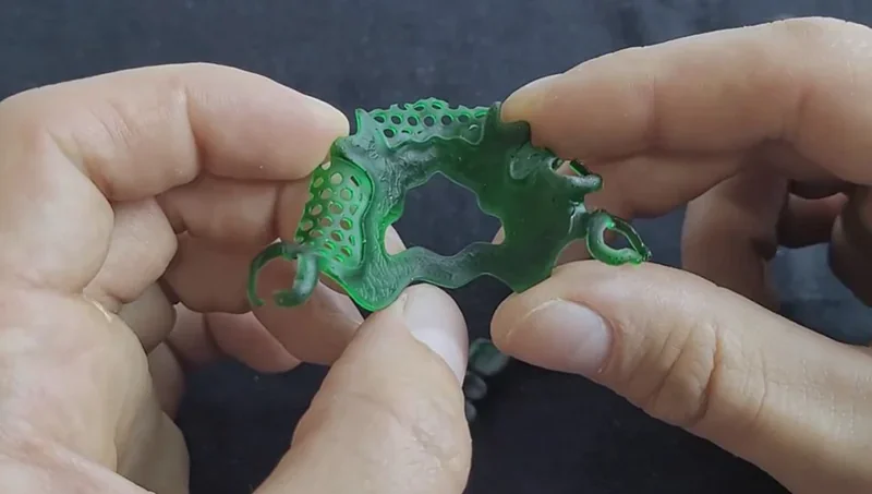 Person holds intricate green resin model created by Phrozen Sonic XL 4K Plus 3D printer, showcasing detailed latticework on black background.