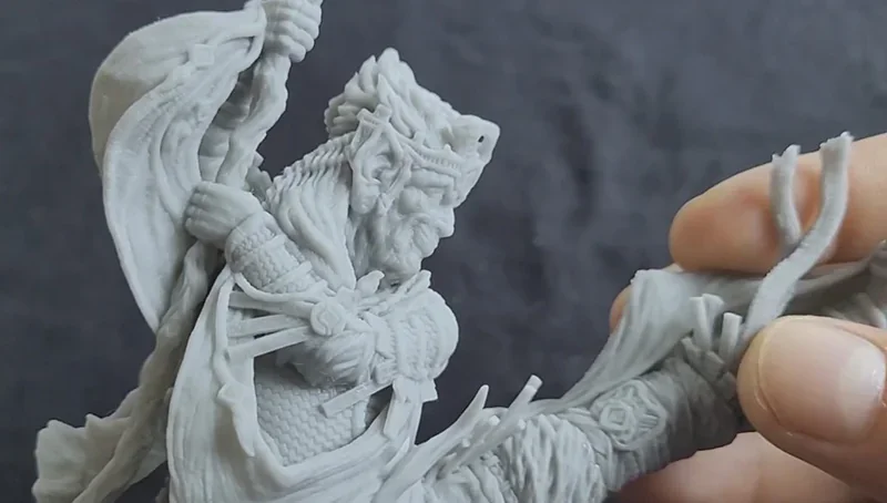 Detailed gray 3D-printed figurine of a warrior holding fabric, created by Phrozen Sonic XL 4K Plus. Hands show scale and detail against a dark background.