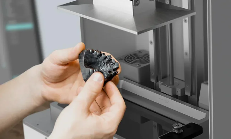 Hands holding dental model near Phrozen Sonic XL 4K Plus 3D printer, showcasing precision printing capabilities.