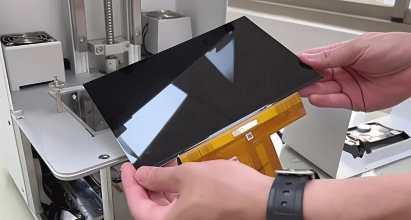 Open Phrozen Sonic XL 4K Plus printer with user handling black build plate, showing interior components. Parts made by this printer, modern design.