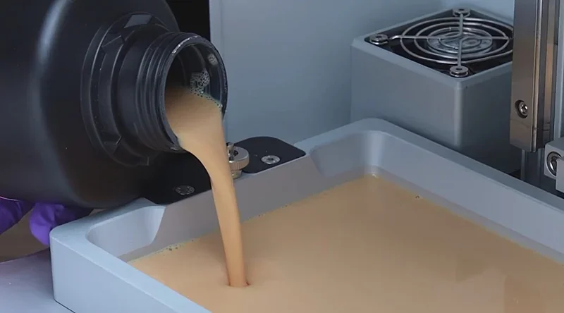 Phrozen Sonic XL 4K Plus 3D printer with resin being poured into the tray, gray machine parts visible, ready for high-resolution printing.