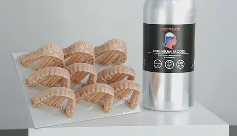 Phrozen Sonic XL 4K Plus 3D-printed dental models next to Liqcreate Premium Model resin bottle on white surface.