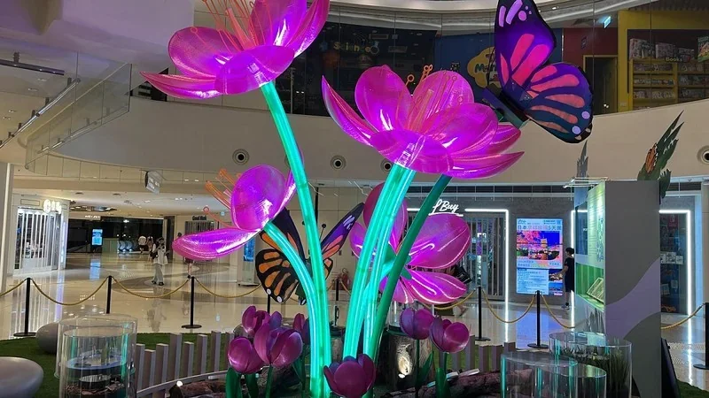 Piocreat G12 3D-printed vibrant, pink glowing flowers and a colorful butterfly in a lit indoor display at a commercial setting.