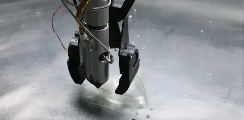 Piocreat G12 3D printer extruder creating a layered part on a smooth metallic surface, showcasing precision and advanced printing technology.