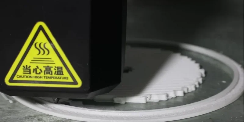 Piocreat G12 3D printer creating circular white part, caution sign displays elevated temperature warning.