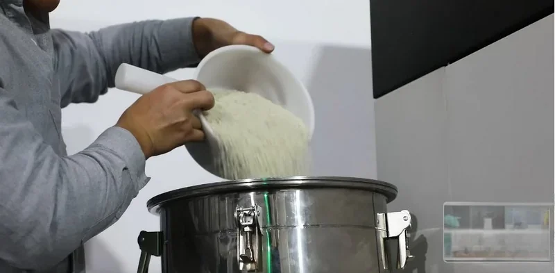Person pouring material into piocreat g12 3D printer, focusing on stainless steel container, suggesting setup or material loading process.