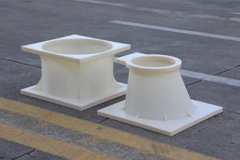 Two large, white, 3D-printed duct parts made by piocreat g12 on a concrete surface with yellow lines.