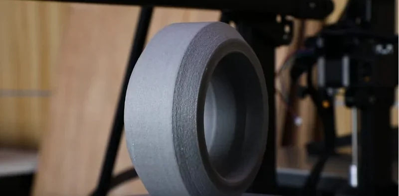 Piocreat G5 print showing a smooth, cylindrical object in a workshop setting with 3D printer machinery in the background.