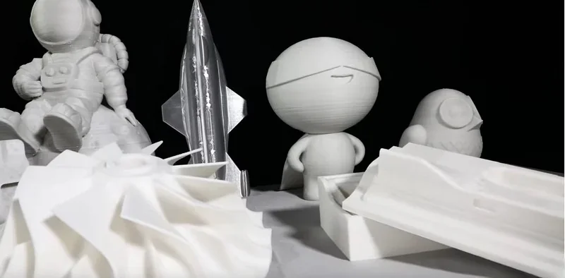 3D-printed astronaut, rocket, and figures created by Piocreat G5 displayed with mold parts on a black background.