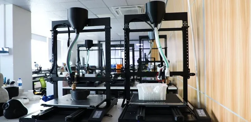 Piocreat G5 3D printers in an office setting, showcasing printed parts. Two printers are working, each with visible nozzles and filament tubes.
