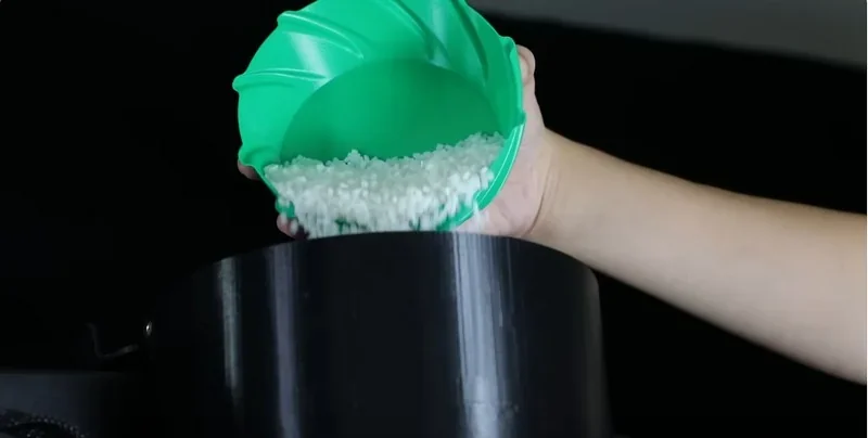 Hand pouring grains into a black container, illustrating material use for piocreat g5 3D printer. Green scoop adds to focus in this close-up.