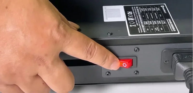 Finger pressing power switch on Piocreat G5 3D printer, with visible branding and specifications label on the device's black metal surface.