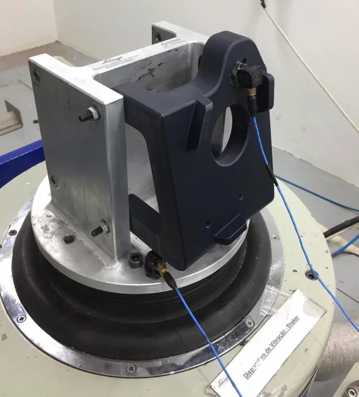 Piocreat G5-created black 3D printed part mounted on a metal rig with visible wires, in a workshop setting, showcasing professional manufacturing.