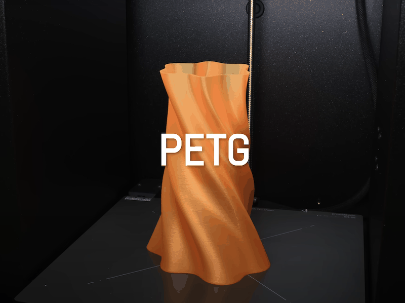 A 3D-printed object created by the Prusa Core One, showcasing an angular, vase-like shape in a vibrant orange PETG filament. The object exhibits smooth curves and a glossy finish, indicating high-quality printing. The background shows the interior of a 3D printer with a textured black surface. The text “PETG” is prominently displayed over the object to highlight the material used.