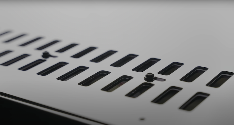 The image displays a close-up of a black surface with several rectangular slots. Two small fasteners or screws are visible on the surface, likely part of the printer's exterior or