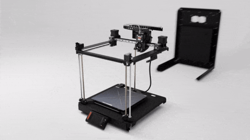 The image shows the Prusa Core One 3D printer with its open frame design. It features a sturdy black metal frame with linear rails and a central print head for stable movement. The print bed is positioned at the bottom with a sleek, black surface, and an attached control panel is located at the front. The background is minimal, emphasizing the printer's mechanical components and assembly.