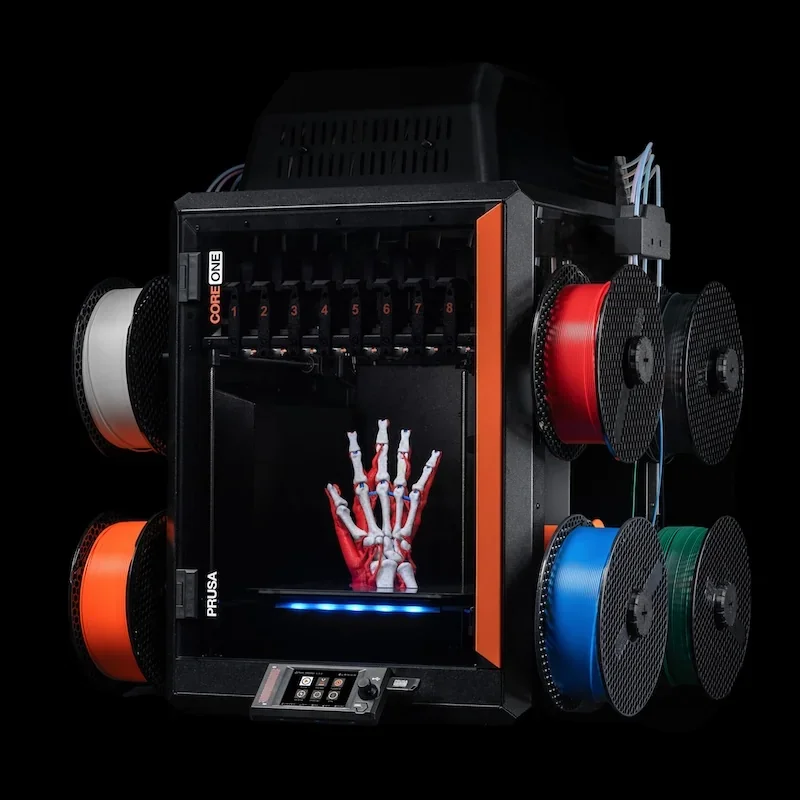 Prusa Core One 3D printer with multicolored filament spools and a skeletal hand print sample inside, showcasing advanced multi-material printing capabilities.