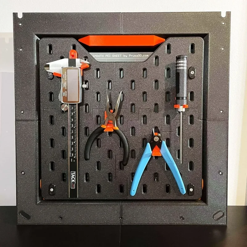 A tool organizer, possibly created using a 3D printer like the Prusa Core One, is mounted on a wall. The board is black with a perforated design and showcases various tools neatly attached, including a caliper, pliers, a screwdriver, and cutters. The organizer features elements in orange, which may be indicative of Prusa's branding. The smooth PEI sheet branding of Prusa3D.com is visible, suggesting high-quality materials or accessories used for 3D printing.