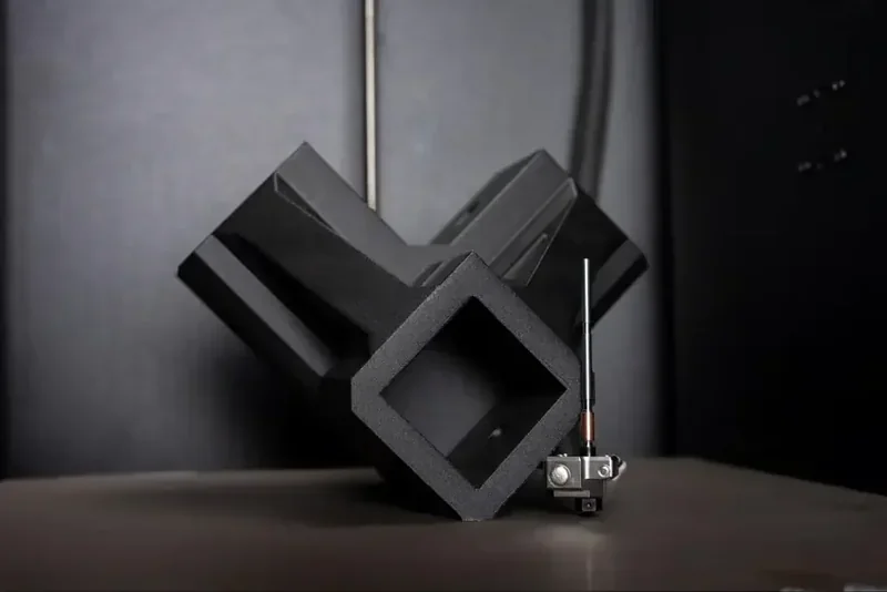 Prusa Core One 3D printed black geometric part, showcasing precision and detail, set on a flat surface in a professional 3D printer environment.